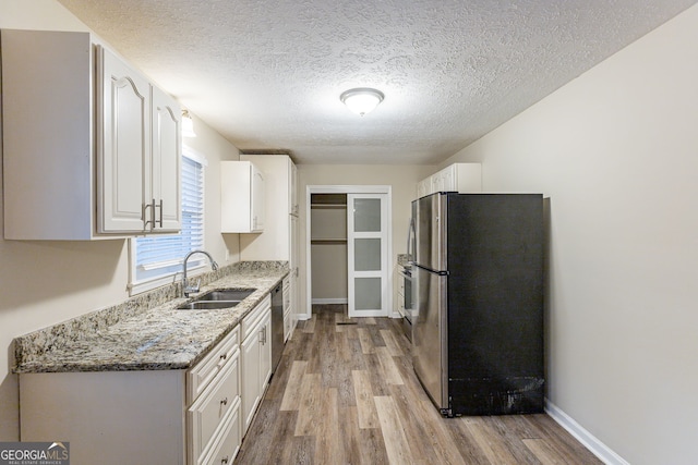 kitchen with stainless steel appliances, light stone counters, white cabinets, sink, and light hardwood / wood-style flooring