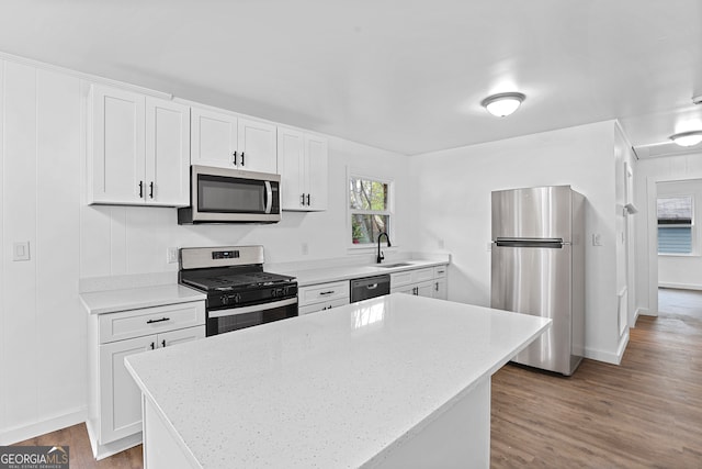 kitchen with stainless steel appliances, white cabinetry, sink, hardwood / wood-style flooring, and a center island