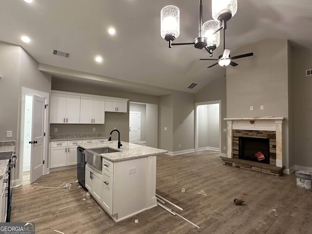 kitchen with an island with sink, light stone countertops, a fireplace, sink, and white cabinetry