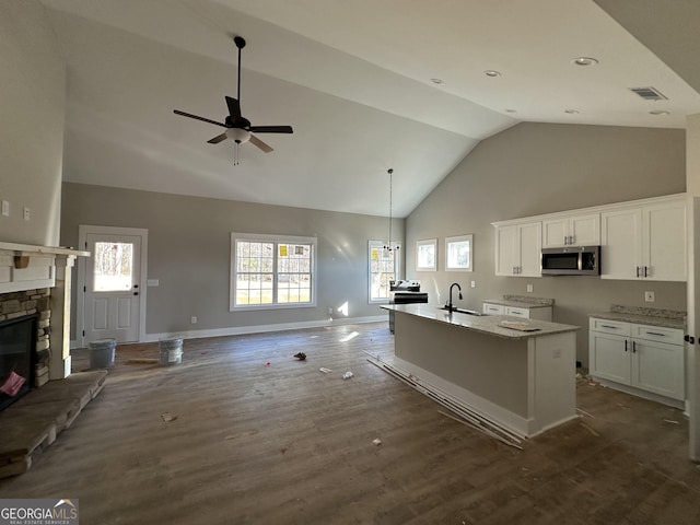 kitchen with white cabinets, a kitchen island with sink, light stone countertops, and a fireplace