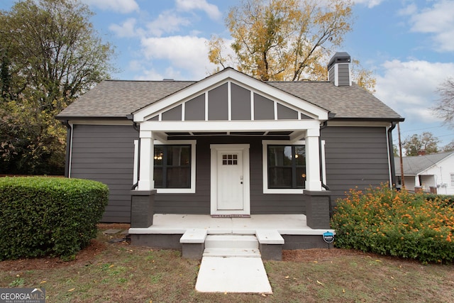 bungalow-style home featuring a porch, a chimney, and a shingled roof