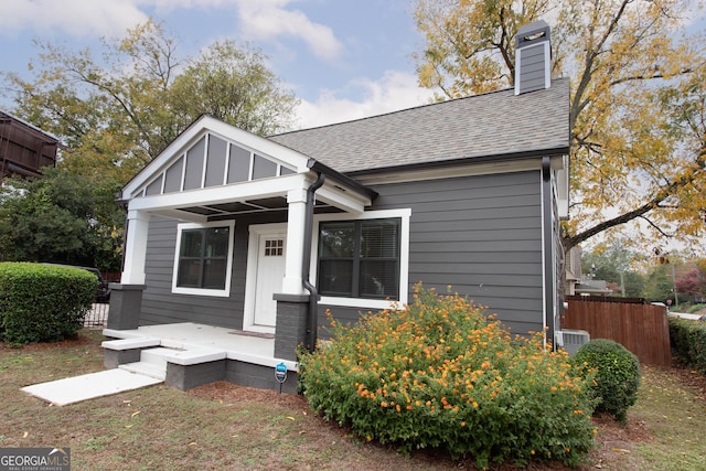 bungalow-style home with a porch, cooling unit, fence, roof with shingles, and a chimney