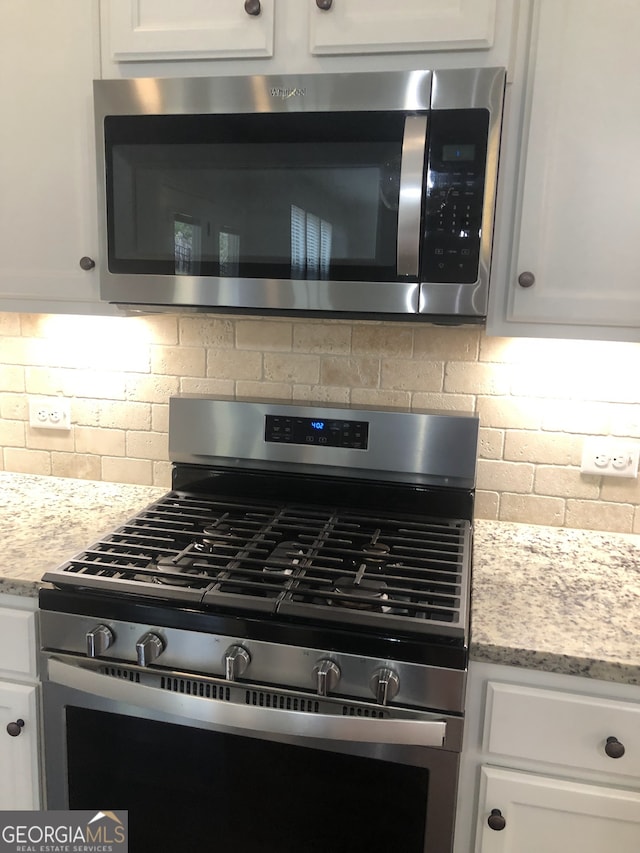 details with stainless steel appliances, light stone countertops, white cabinetry, and backsplash