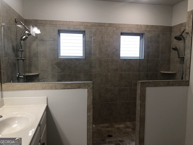 bathroom with vanity, a tile shower, and a healthy amount of sunlight