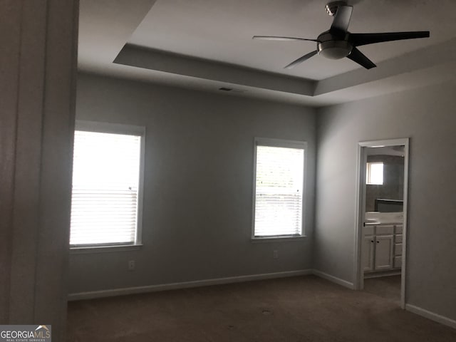 empty room featuring dark colored carpet, ceiling fan, and a tray ceiling