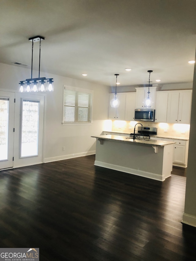 kitchen featuring white cabinets, hanging light fixtures, dark wood-type flooring, and an island with sink