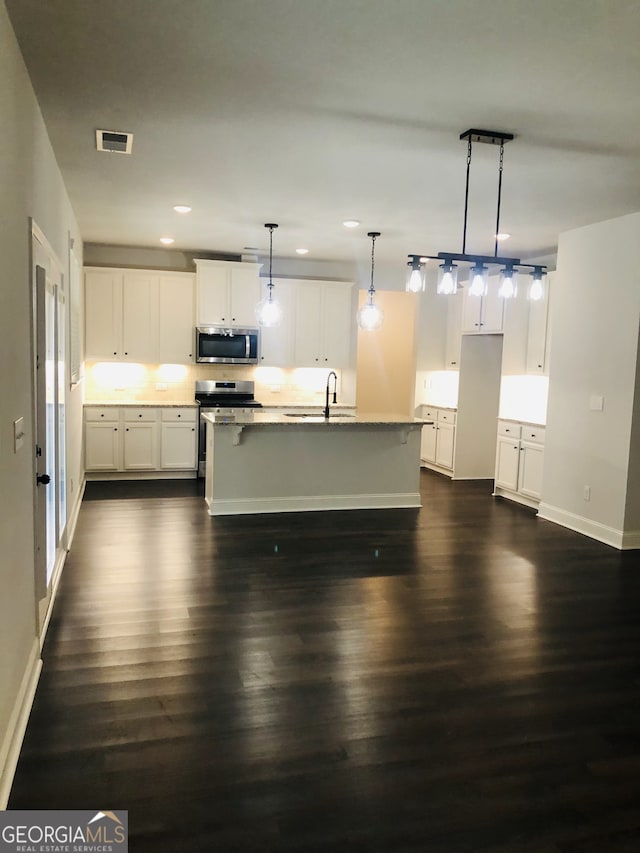 kitchen featuring a center island with sink, white cabinetry, appliances with stainless steel finishes, dark hardwood / wood-style flooring, and pendant lighting