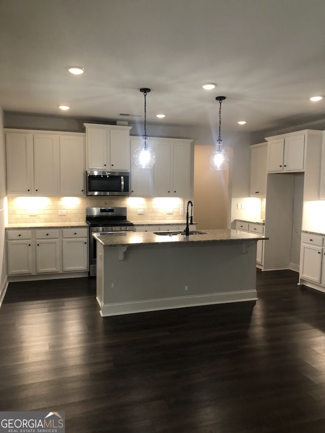 kitchen featuring appliances with stainless steel finishes, decorative light fixtures, dark hardwood / wood-style floors, sink, and a kitchen island with sink