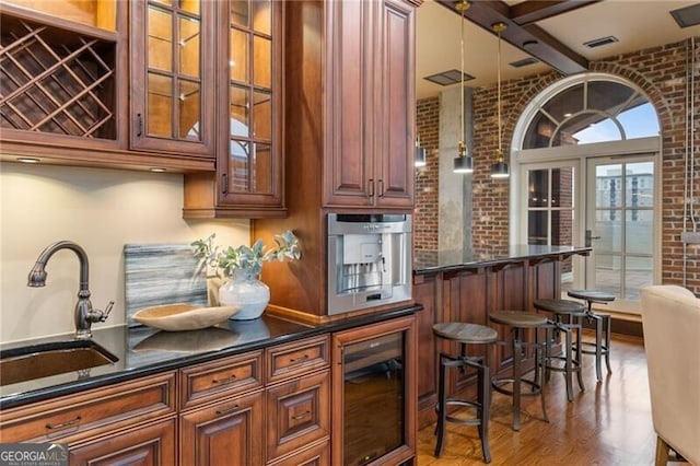 bar with beverage cooler, sink, hardwood / wood-style flooring, beamed ceiling, and brick wall