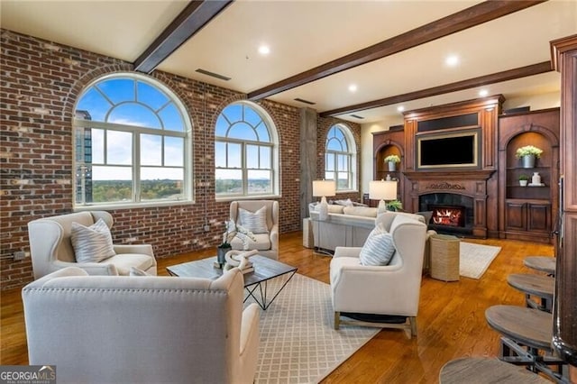 living room featuring light hardwood / wood-style flooring, brick wall, beamed ceiling, and plenty of natural light