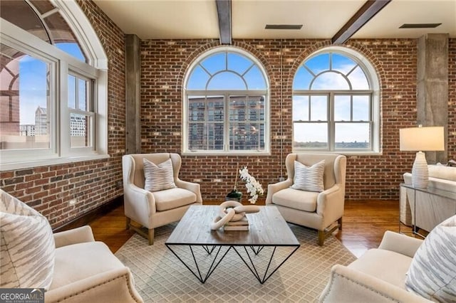 sitting room with beam ceiling, hardwood / wood-style flooring, and brick wall