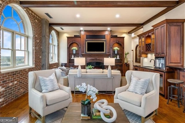 living room featuring beamed ceiling, sink, dark hardwood / wood-style floors, and brick wall