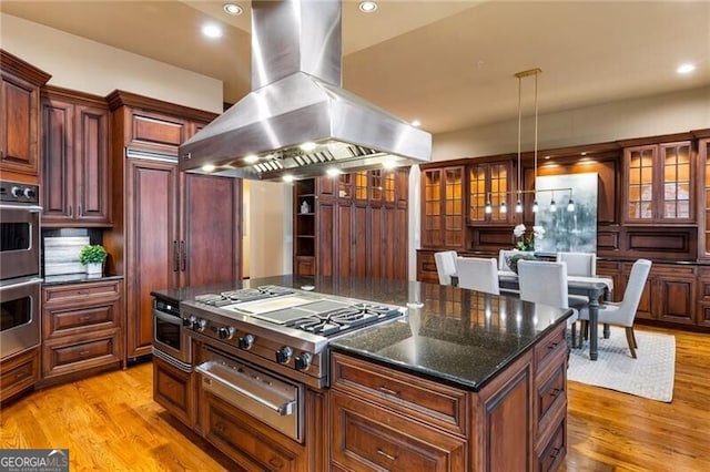 kitchen with island range hood, stainless steel appliances, a kitchen island, decorative light fixtures, and light hardwood / wood-style floors