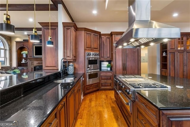 kitchen with sink, dark stone countertops, island range hood, decorative light fixtures, and light wood-type flooring