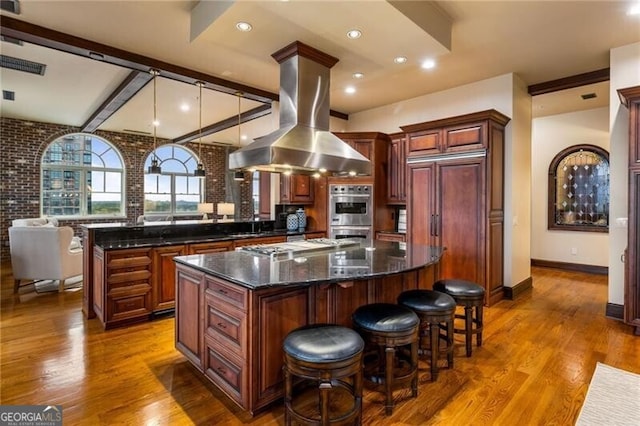 kitchen with dark hardwood / wood-style flooring, a kitchen island, island exhaust hood, and appliances with stainless steel finishes