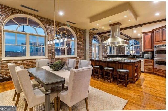 dining space featuring light hardwood / wood-style floors, brick wall, and sink