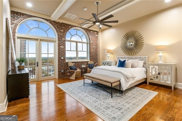 bedroom featuring beam ceiling, hardwood / wood-style flooring, ceiling fan, and brick wall