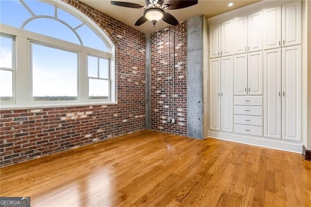 unfurnished bedroom with light hardwood / wood-style floors, brick wall, and ceiling fan