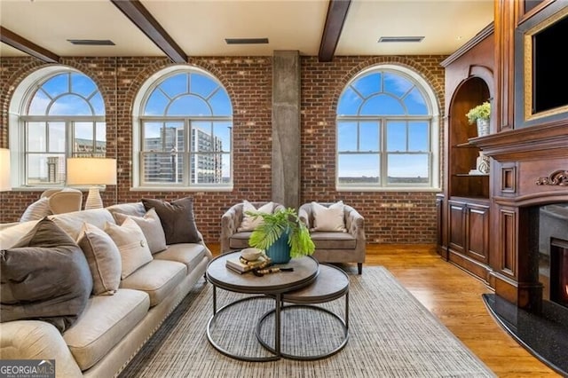 living room featuring a wealth of natural light, beam ceiling, brick wall, and light hardwood / wood-style flooring