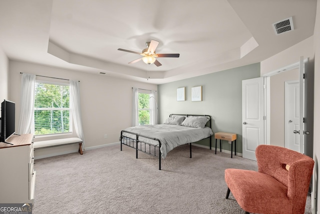 bedroom featuring a tray ceiling, baseboards, multiple windows, and visible vents