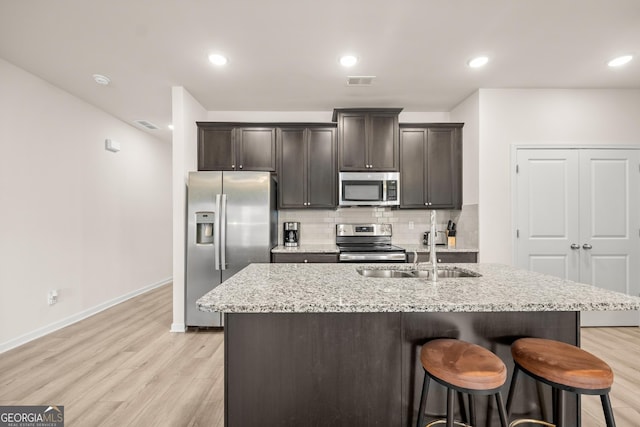 kitchen with a breakfast bar, a sink, backsplash, stainless steel appliances, and light wood finished floors