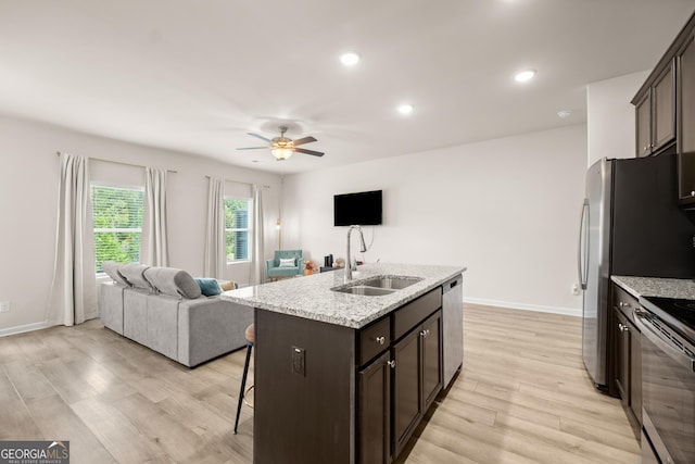 kitchen with dark brown cabinets, open floor plan, a kitchen bar, stainless steel appliances, and a sink