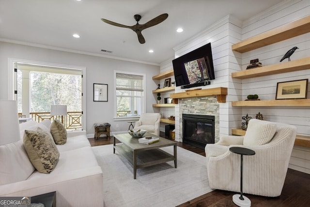 living room with a stone fireplace, ceiling fan, hardwood / wood-style floors, and ornamental molding