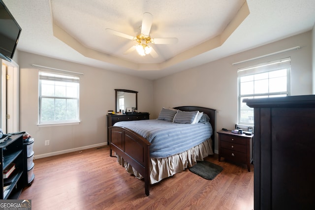 bedroom featuring hardwood / wood-style floors, ceiling fan, a textured ceiling, and a tray ceiling