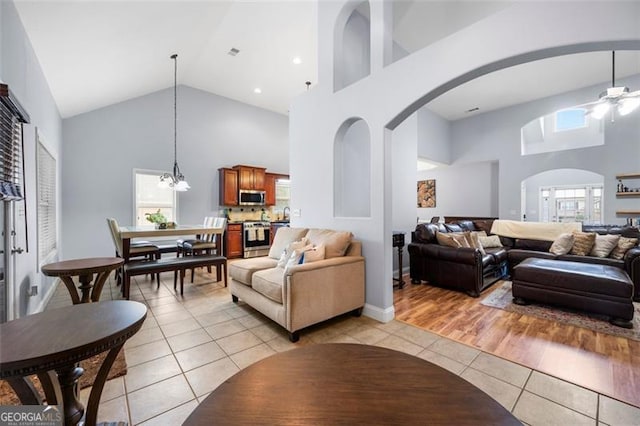 living room with high vaulted ceiling, light tile patterned flooring, and ceiling fan with notable chandelier