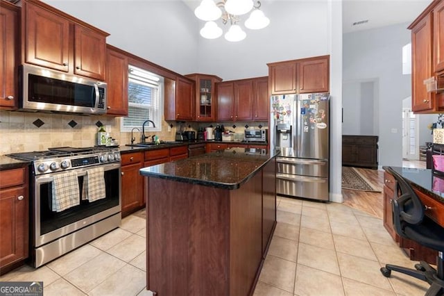 kitchen featuring stainless steel appliances, dark stone counters, a kitchen island, sink, and a chandelier