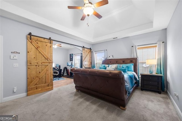 carpeted bedroom with a barn door, ceiling fan, and a raised ceiling