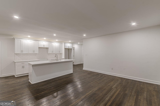 kitchen with a kitchen island with sink, dark wood-type flooring, sink, tasteful backsplash, and white cabinetry