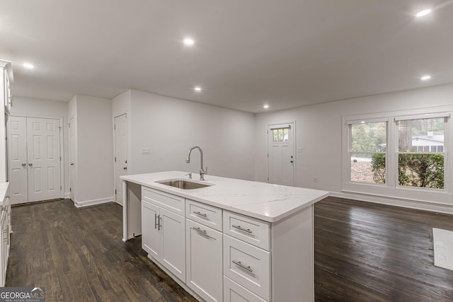 kitchen featuring light stone counters, a kitchen island with sink, dark wood-type flooring, sink, and white cabinets