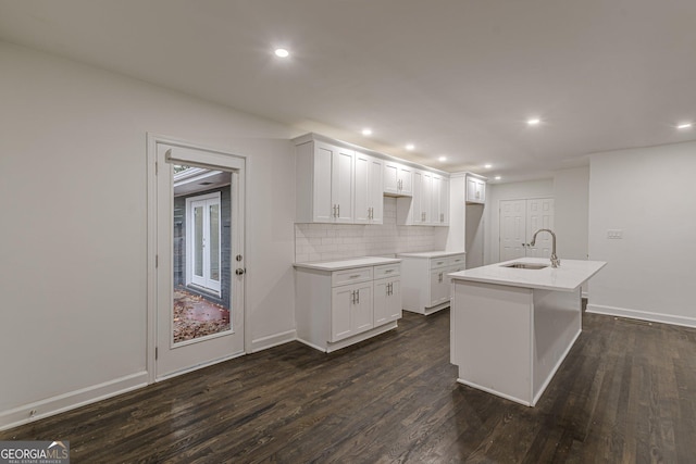 kitchen featuring tasteful backsplash, dark wood-type flooring, sink, white cabinets, and an island with sink