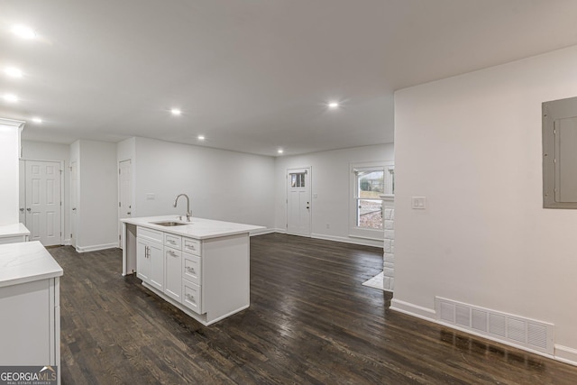 kitchen featuring electric panel, white cabinets, sink, an island with sink, and dark hardwood / wood-style flooring