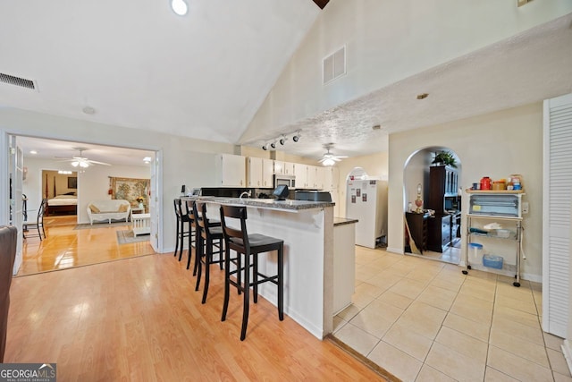 kitchen with a breakfast bar, white refrigerator, light hardwood / wood-style flooring, dark stone countertops, and white cabinets