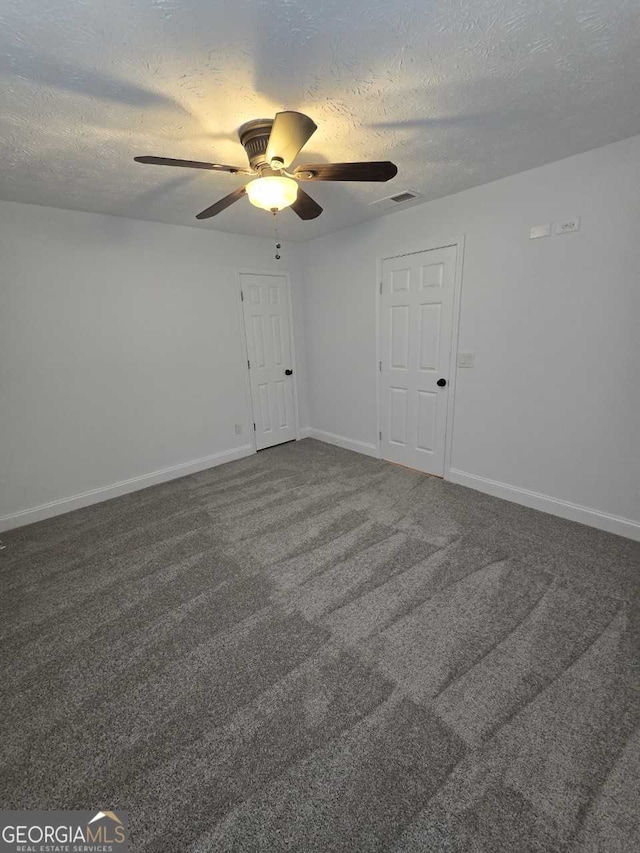 empty room featuring a textured ceiling, ceiling fan, and dark carpet