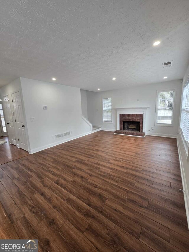 unfurnished living room featuring a textured ceiling, a brick fireplace, and dark hardwood / wood-style floors