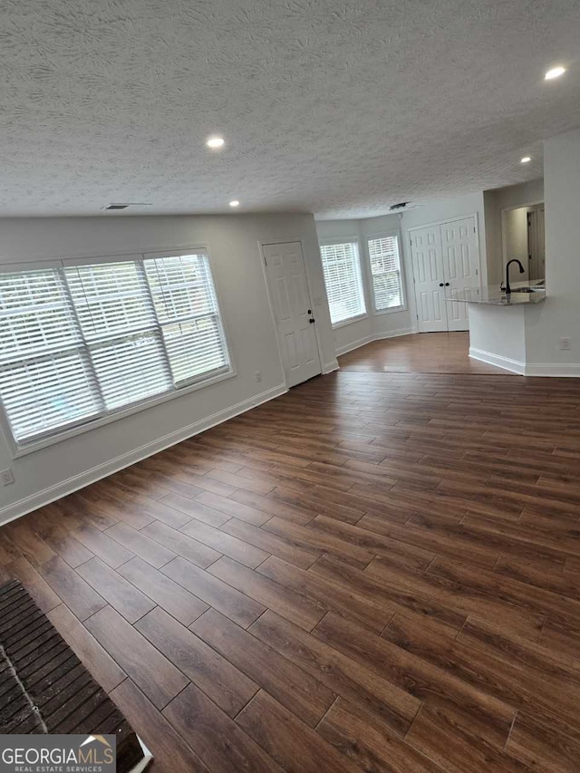 unfurnished living room with dark wood-type flooring, a textured ceiling, and sink