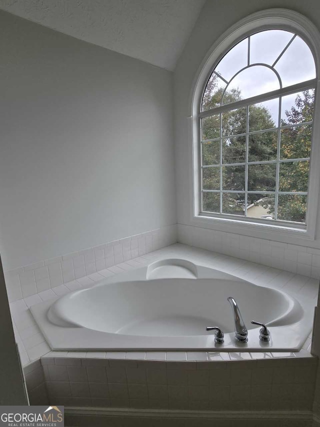 bathroom featuring a relaxing tiled tub, a textured ceiling, and lofted ceiling