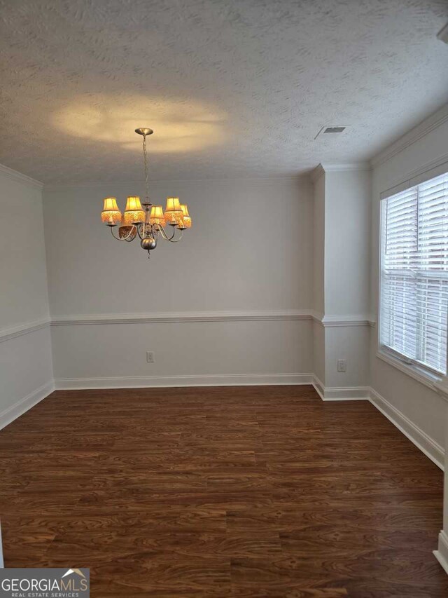 spare room featuring a textured ceiling, ornamental molding, dark hardwood / wood-style floors, and an inviting chandelier