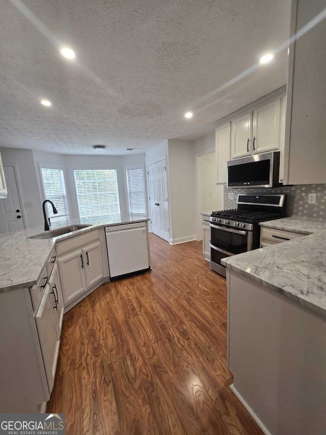 kitchen with light stone counters, stainless steel appliances, sink, white cabinets, and dark wood-type flooring