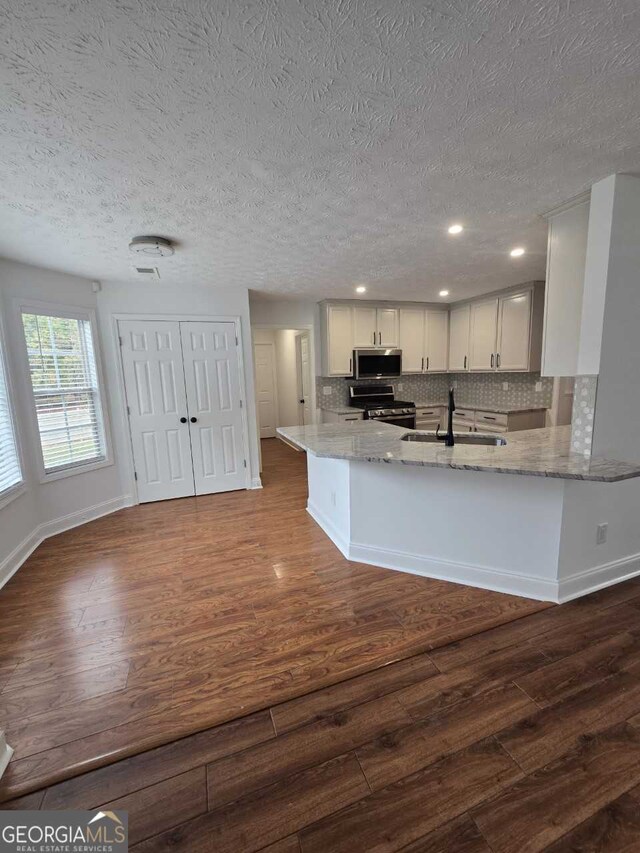 kitchen featuring light stone counters, dark hardwood / wood-style flooring, sink, white cabinets, and kitchen peninsula