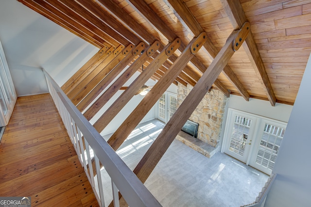 stairs with french doors, vaulted ceiling with beams, a fireplace, hardwood / wood-style floors, and wooden ceiling