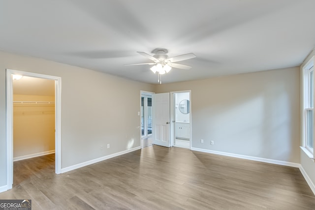 unfurnished bedroom with a closet, a walk in closet, light hardwood / wood-style flooring, ceiling fan, and ensuite bathroom