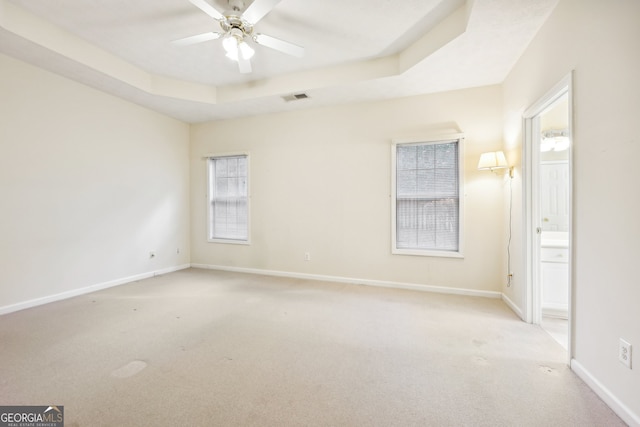 carpeted empty room with ceiling fan and a raised ceiling