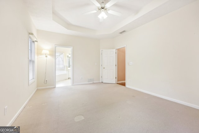 unfurnished bedroom featuring a raised ceiling, connected bathroom, ceiling fan, and light colored carpet