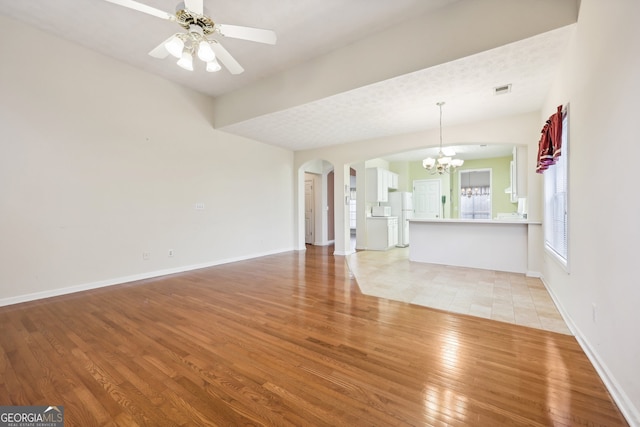 unfurnished living room with a textured ceiling, ceiling fan with notable chandelier, light hardwood / wood-style floors, and lofted ceiling