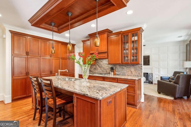 kitchen with decorative light fixtures, light hardwood / wood-style floors, sink, and a center island with sink