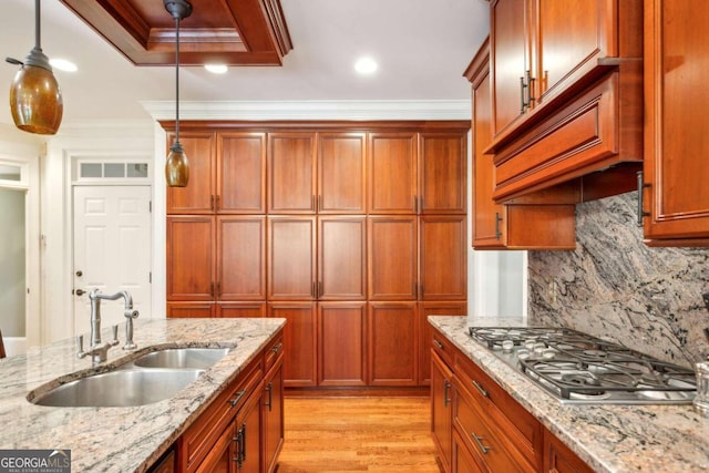 kitchen featuring hanging light fixtures, stainless steel gas stovetop, sink, and light stone countertops